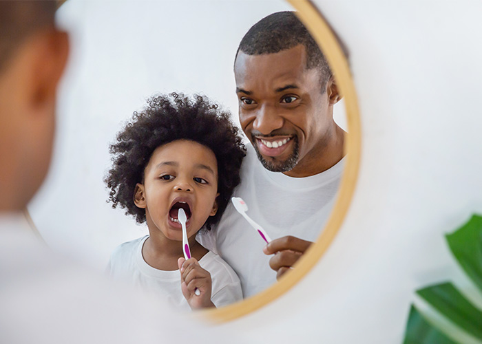father and child brushing teeth while looking in mirror