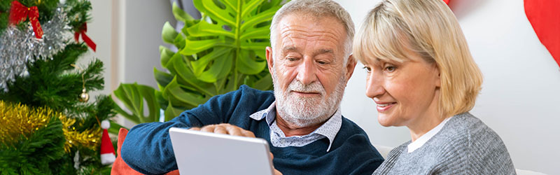 happy senior couple sitting on couch looking at ipad