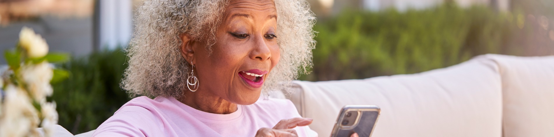 senior woman sitting in garden making video call on cell phone