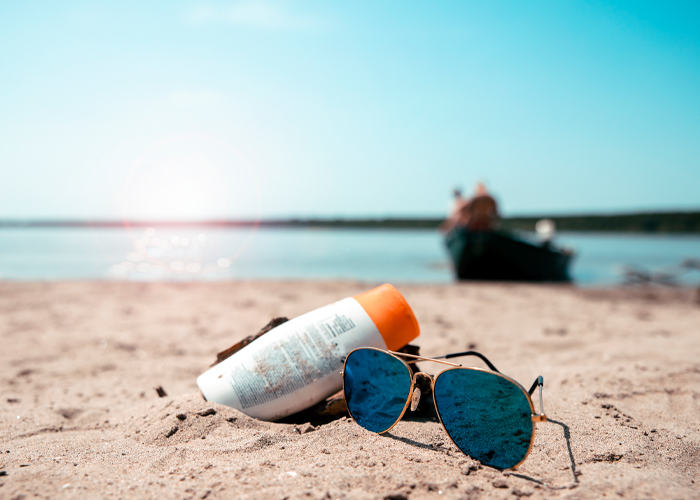 sunglasses and sun lotion on sandy beach